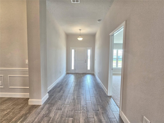 entrance foyer featuring a textured wall, dark wood-style floors, baseboards, and visible vents