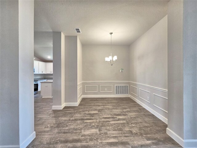 unfurnished dining area featuring visible vents, a decorative wall, dark wood-type flooring, and a chandelier