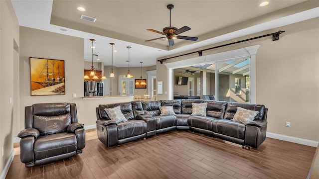 living room with ceiling fan, a raised ceiling, and wood-type flooring