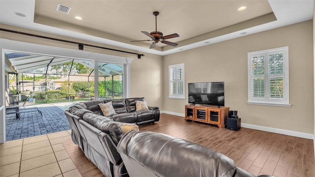 living room with ceiling fan, a tray ceiling, and hardwood / wood-style floors