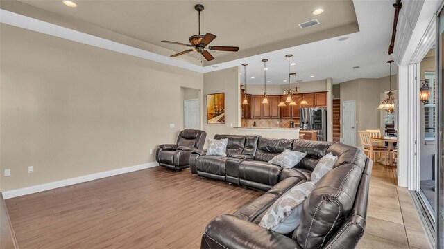 living room with a tray ceiling, light wood-type flooring, and ceiling fan with notable chandelier