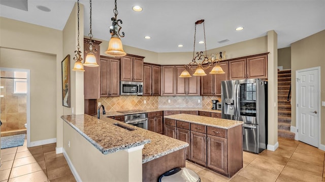 kitchen with light stone countertops, appliances with stainless steel finishes, light tile patterned flooring, a kitchen bar, and pendant lighting