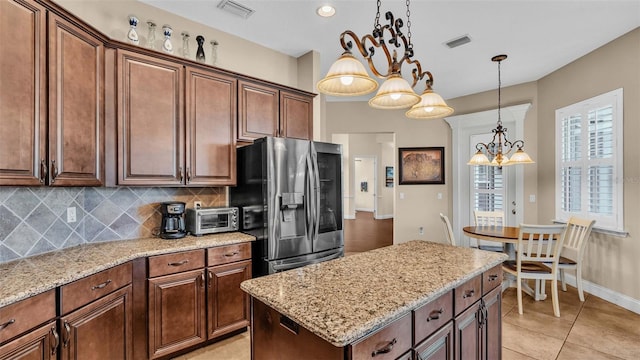 kitchen with light stone countertops, a kitchen island, hanging light fixtures, stainless steel fridge, and light tile patterned floors