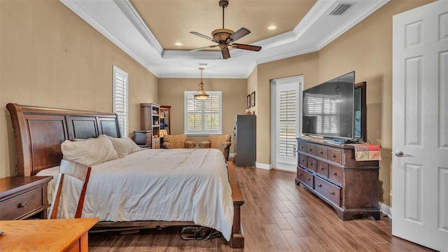 bedroom with crown molding, wood-type flooring, a tray ceiling, and ceiling fan