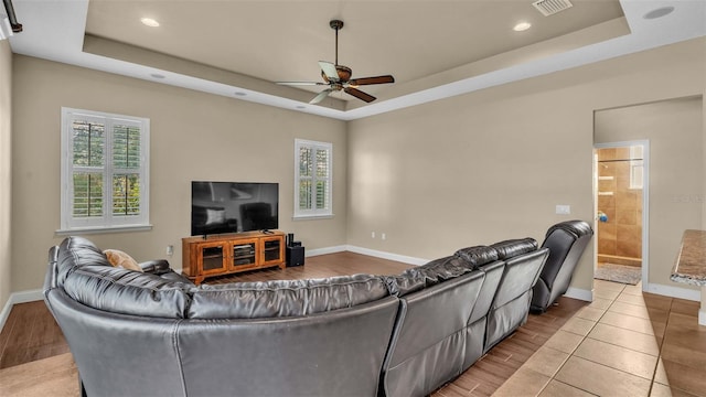 living room with ceiling fan, light wood-type flooring, and a raised ceiling