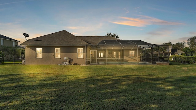 back house at dusk featuring a lawn and glass enclosure