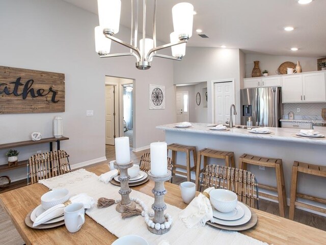 dining space featuring a notable chandelier, high vaulted ceiling, sink, and dark hardwood / wood-style flooring