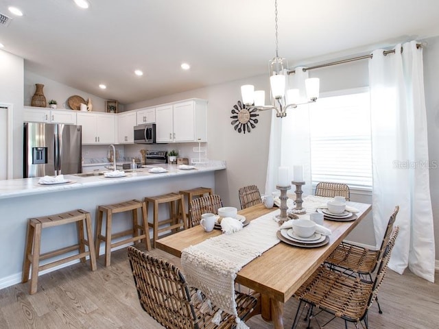 dining room featuring light hardwood / wood-style floors, an inviting chandelier, sink, and vaulted ceiling