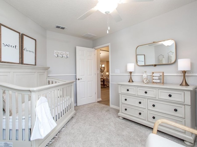 carpeted bedroom featuring a nursery area, a textured ceiling, and ceiling fan