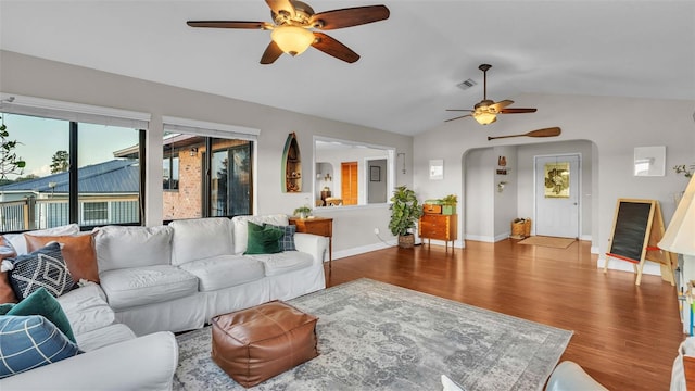 living area with arched walkways, lofted ceiling, visible vents, wood finished floors, and baseboards