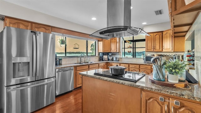 kitchen featuring light stone counters, brown cabinets, island exhaust hood, appliances with stainless steel finishes, and a sink