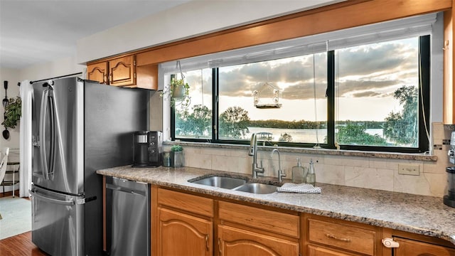 kitchen featuring stainless steel appliances, brown cabinetry, a sink, and backsplash