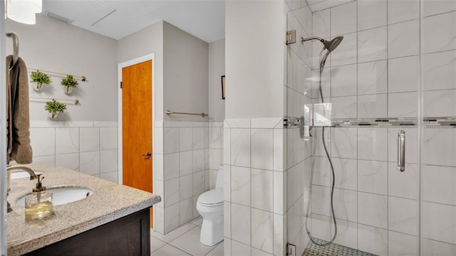 bathroom with tile walls, toilet, a stall shower, vanity, and tile patterned floors