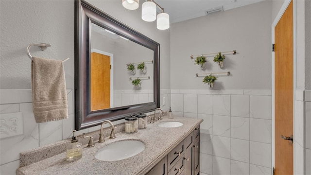 bathroom featuring double vanity, visible vents, tile walls, and a sink