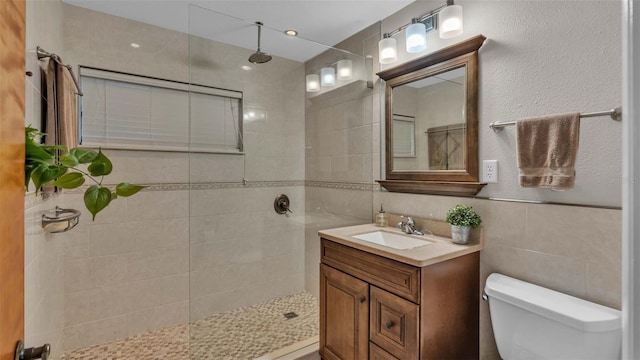 bathroom with vanity, toilet, tile walls, and tiled shower