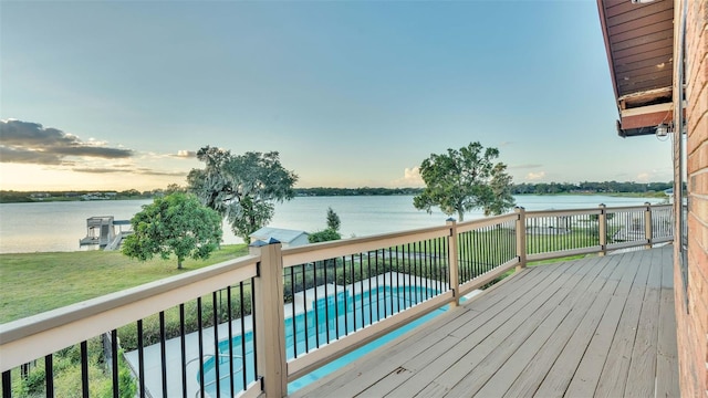 wooden deck with a fenced in pool, a water view, and a lawn