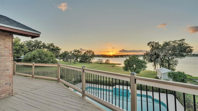 deck at dusk featuring a fenced in pool and a water view