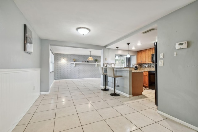 kitchen featuring kitchen peninsula, a kitchen breakfast bar, black appliances, light tile patterned floors, and hanging light fixtures