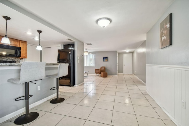 kitchen with a kitchen breakfast bar, light stone counters, decorative light fixtures, light tile patterned floors, and black appliances