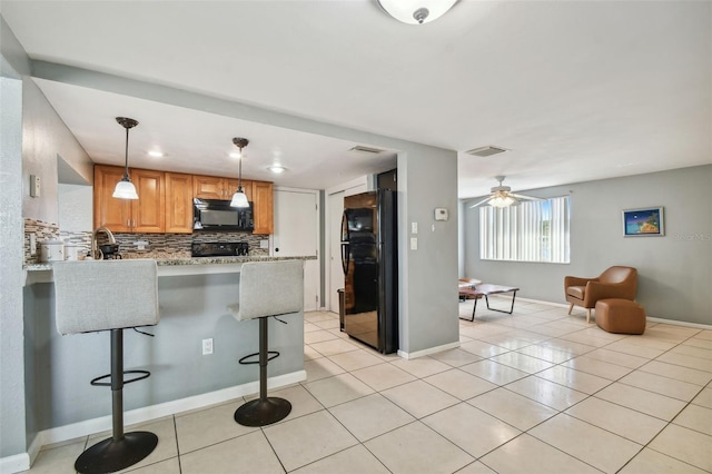 kitchen with a kitchen bar, light tile patterned flooring, pendant lighting, black appliances, and kitchen peninsula