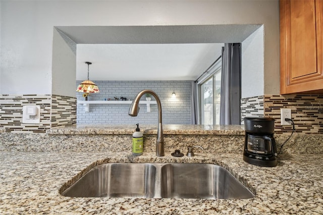 kitchen featuring decorative backsplash, sink, light stone counters, and decorative light fixtures