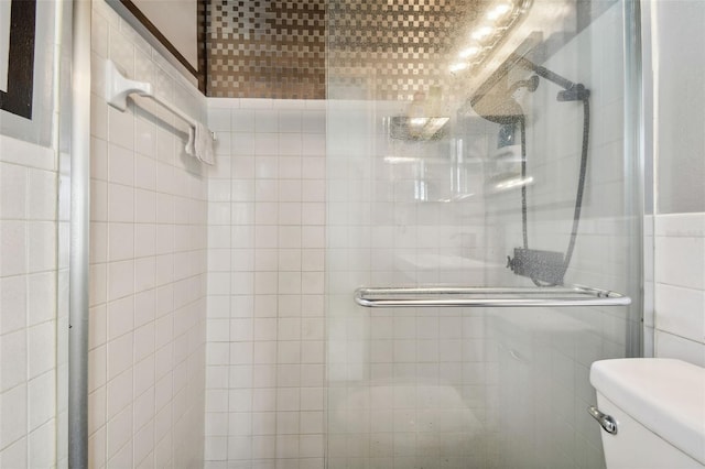 bathroom featuring toilet, tile walls, and a shower with door