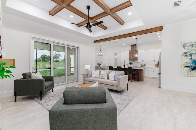 living room featuring ceiling fan with notable chandelier, coffered ceiling, beamed ceiling, ornamental molding, and light hardwood / wood-style flooring