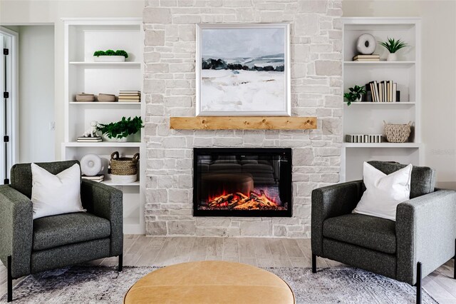 sitting room featuring a stone fireplace, wood-type flooring, and built in shelves