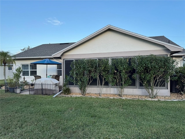 back of house featuring a shingled roof, a lawn, a sunroom, and stucco siding