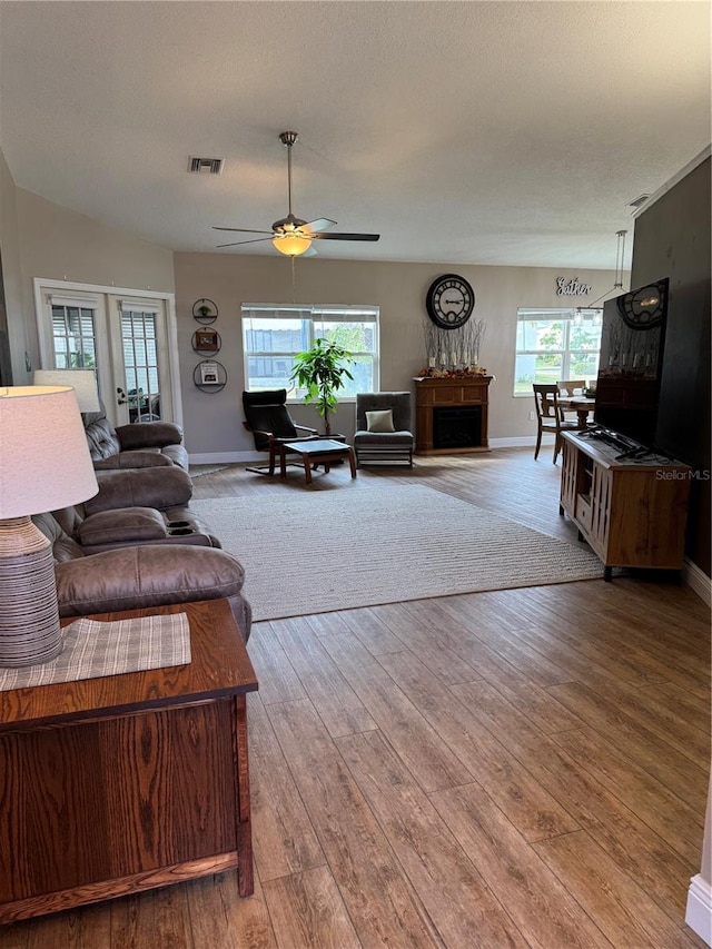 living area featuring ceiling fan, a textured ceiling, wood finished floors, visible vents, and baseboards