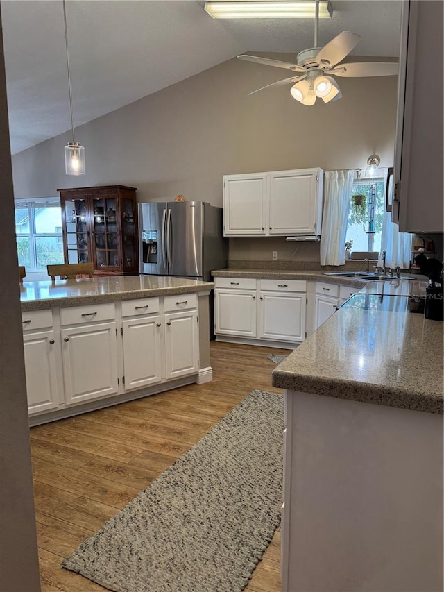 kitchen with stainless steel fridge with ice dispenser, vaulted ceiling, light wood-type flooring, white cabinetry, and a sink