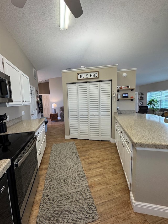 kitchen with stainless steel microwave, electric range, light wood-style floors, white cabinetry, and a peninsula