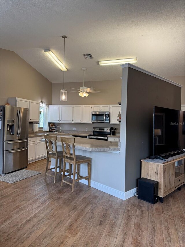 kitchen featuring wood finished floors, visible vents, white cabinetry, hanging light fixtures, and appliances with stainless steel finishes