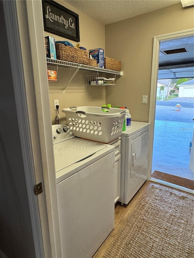 laundry area with washing machine and dryer, laundry area, a textured ceiling, and light wood finished floors