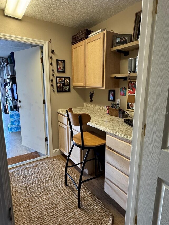 kitchen featuring dark wood-style floors, a textured ceiling, light brown cabinetry, open shelves, and built in desk