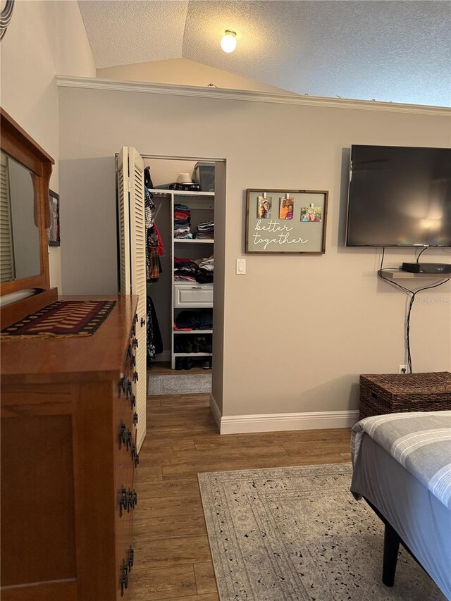 bedroom featuring a textured ceiling, lofted ceiling, wood finished floors, a spacious closet, and a closet