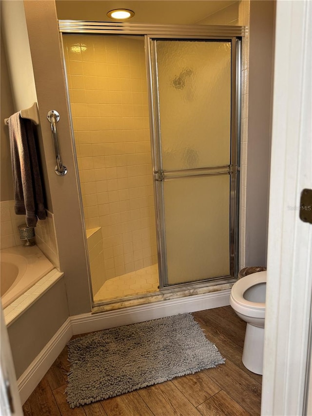 full bath featuring a bath, a shower stall, toilet, and wood finished floors