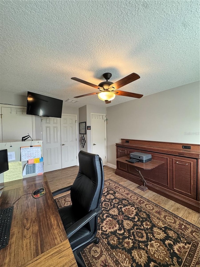 home office with light wood-style flooring, a textured ceiling, and a ceiling fan