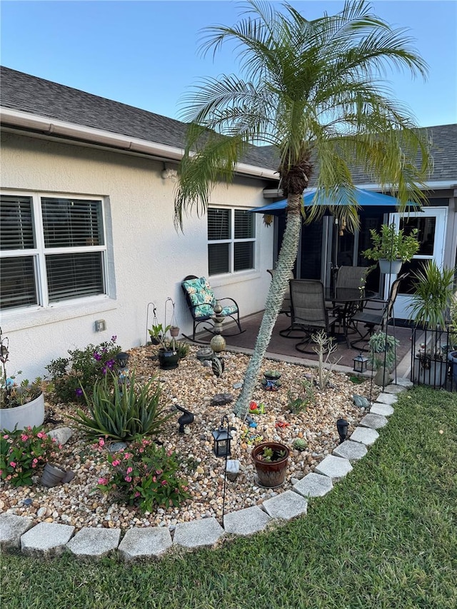 exterior space featuring a shingled roof, a patio area, and stucco siding