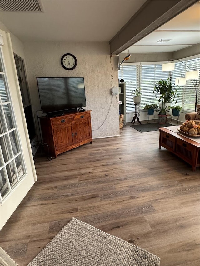 living area featuring visible vents, beamed ceiling, wood finished floors, and a textured wall