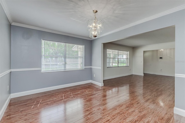 empty room featuring crown molding, hardwood / wood-style floors, a notable chandelier, and plenty of natural light