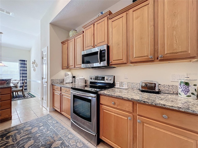 kitchen featuring appliances with stainless steel finishes, light stone counters, pendant lighting, and light tile patterned floors