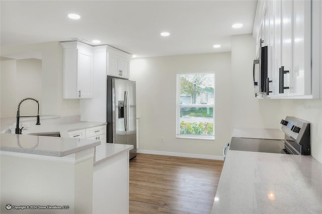 kitchen featuring white cabinetry, sink, stainless steel appliances, light hardwood / wood-style flooring, and kitchen peninsula