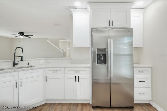 kitchen with white cabinetry, sink, ceiling fan, stainless steel fridge, and light wood-type flooring