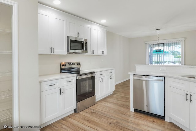 kitchen with appliances with stainless steel finishes, light hardwood / wood-style floors, white cabinetry, and hanging light fixtures