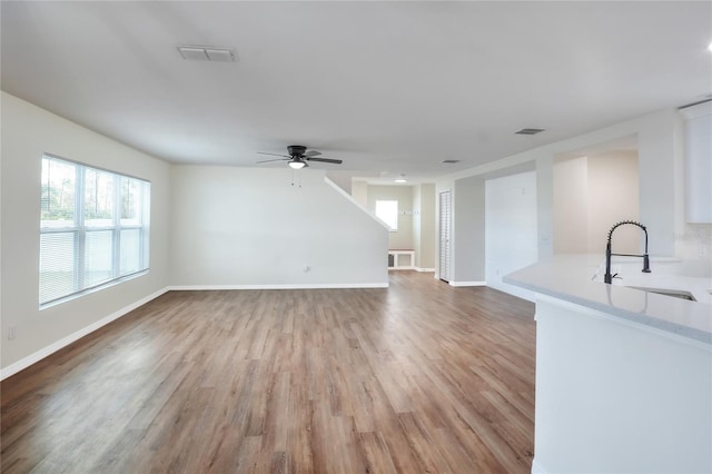 unfurnished living room featuring ceiling fan, sink, and light wood-type flooring