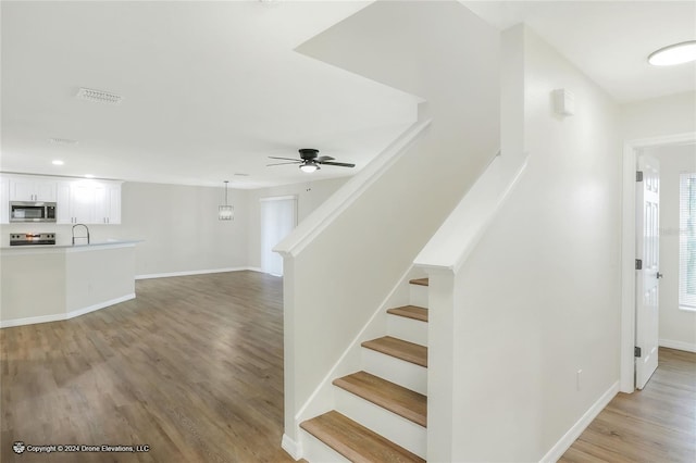 stairway with hardwood / wood-style flooring, ceiling fan, and sink