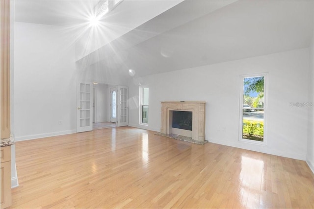 unfurnished living room with french doors, light hardwood / wood-style flooring, lofted ceiling, and a premium fireplace