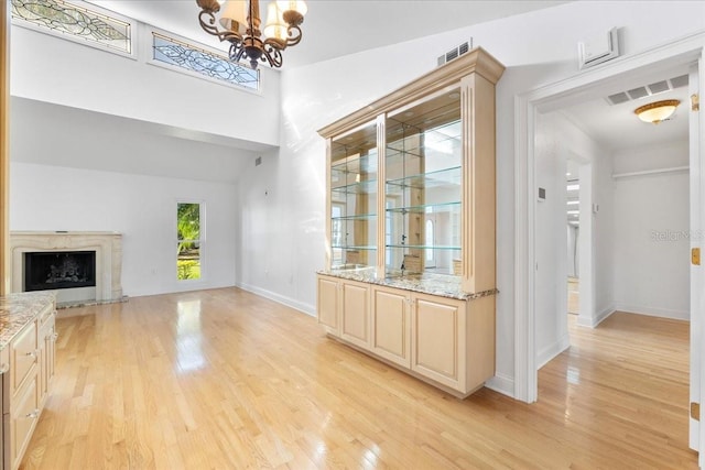 unfurnished living room with a high end fireplace, a chandelier, vaulted ceiling, and light wood-type flooring