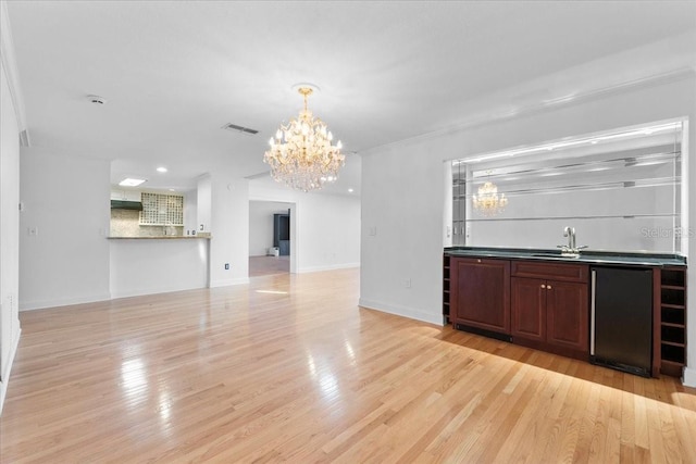 interior space with stainless steel refrigerator, sink, hanging light fixtures, a notable chandelier, and light wood-type flooring